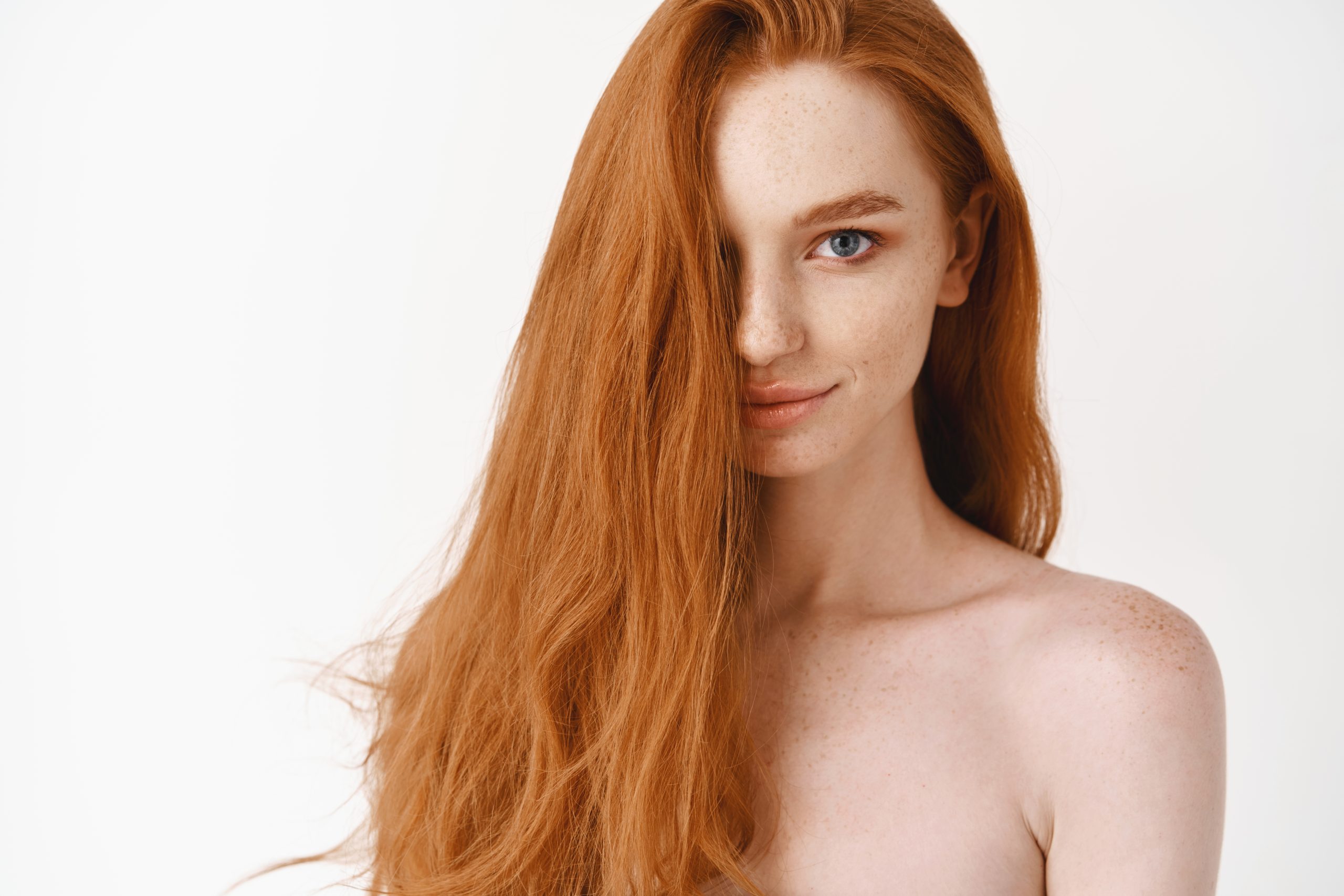 Beautiful young woman with long perfect red hair and blue eyes looking at  camera, standing naked, showing pale clean skin and natural haircut, white  background -